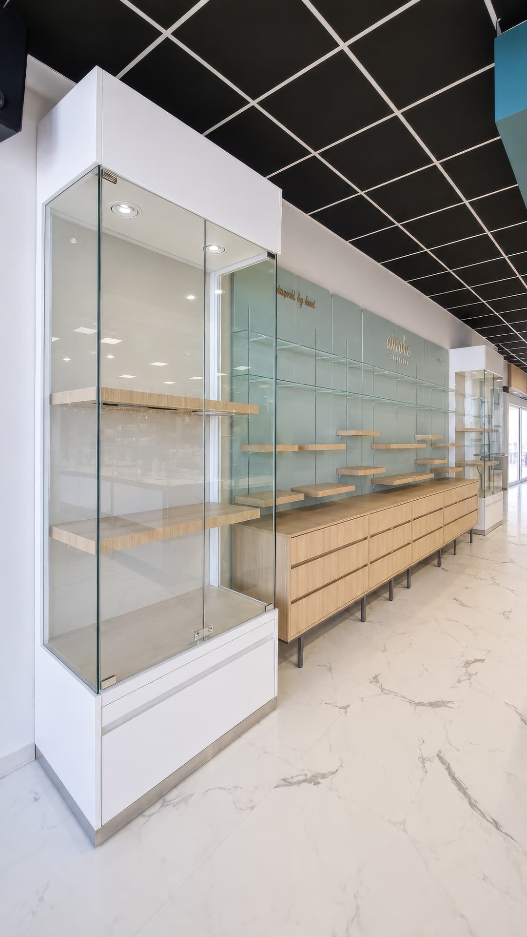 Tall glass vitrine with oak shelves beside a mint display wall